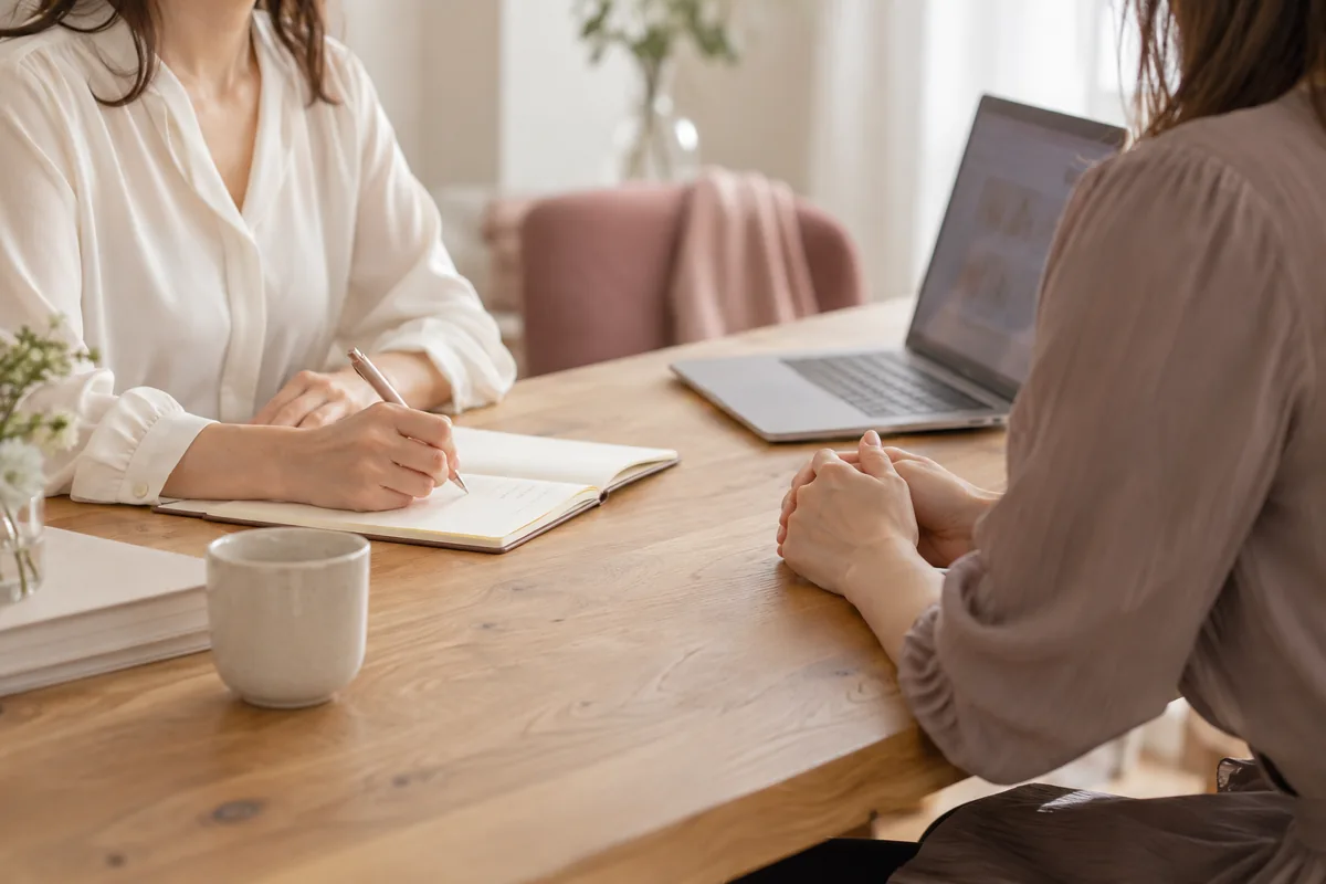 ノートとパソコンを囲み、二人の女性が対話しながら課題を整理する手元のイメージ